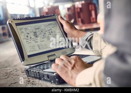 Engineer using laptop,reviewing blueprints in steel mill Stock Photo