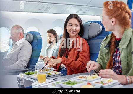 Women friends eating dinner and talking on airplane Stock Photo