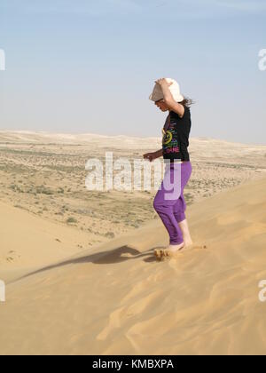 girl standing on sand dune and holding her hat from from the wind in the desert Stock Photo