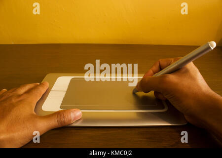 point of view of a male using a silver pen tablet on a brown wood table Stock Photo