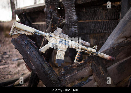 Assault Rifle, painted in sand color on the background of the burnt logs. Airsoft. Stock Photo