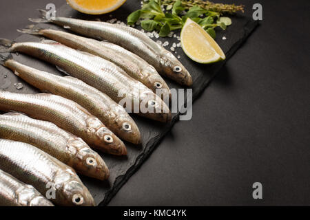 Fresh sea fish smelt or sardines ready for cooking with lemon, thyme, and coarse sea salt on a blue background. The concept of fresh, healthy seafood. Top view Stock Photo