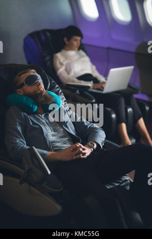 Businessman sleeping while female executive using laptop Stock Photo
