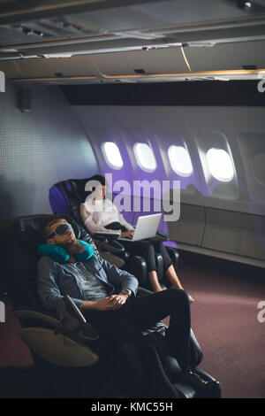 Businessman sleeping while female executive using laptop Stock Photo