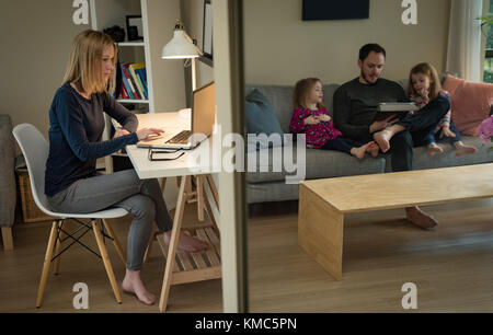 Mother using laptop while father and daughters using digital tablet Stock Photo