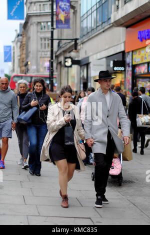 Young man wearing hat walking with woman using smartphone in London, England, UK Stock Photo