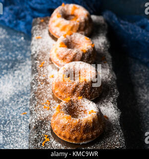 Mini bundt ring cakes with orange zest icing sugar on dark blue background and serving board. Holiday sweet food Stock Photo