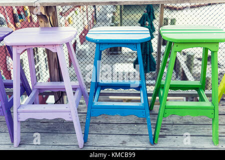 Colorful vivid chairs painted purple, blue and green on waterfront bar restaurant Stock Photo