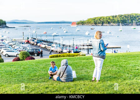 Bar Harbor, USA - June 8, 2017: People, family sitting on green grass hill in park downtown village in summer by boats Stock Photo