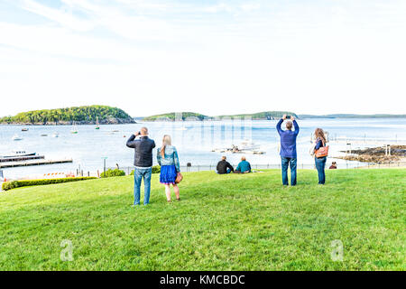 Bar Harbor, USA - June 8, 2017: Young couples taking pictures on green grass hill in park downtown village in summer by boats Stock Photo