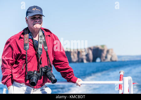 Perce, Canada - June 6, 2017: Professional man photographer with two Olympus cameras on boat by Rocher Perce rock in Gaspe Peninsula, Quebec, Gaspesie Stock Photo