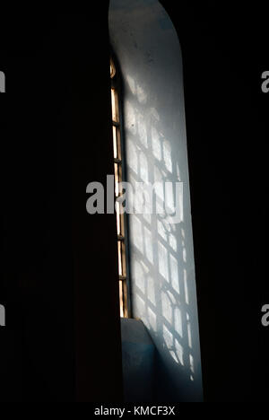 Tall arched window with a vintage metal grille on a black wall, streams of scattered sunlight stream through the window. Stock Photo