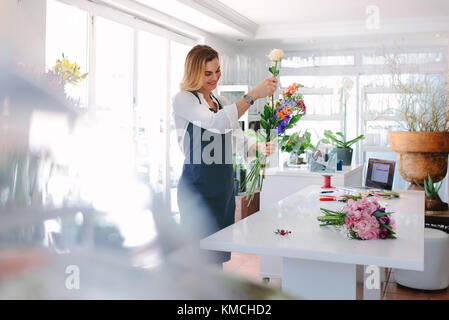 Female florist at work arranging various flowers in bouquet. Woman standing at counter making a bouquet of fresh flowers. Stock Photo