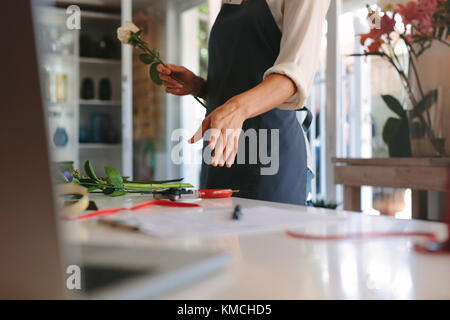 Hands of female working at flower shop arranging flowers. Woman florist making bouquet with flowers on counter. Stock Photo