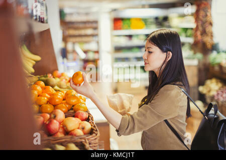 Young woman shopping, examining oranges in grocery store Stock Photo