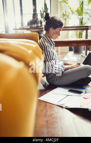 Female freelancer working at laptop on living room floor Stock Photo