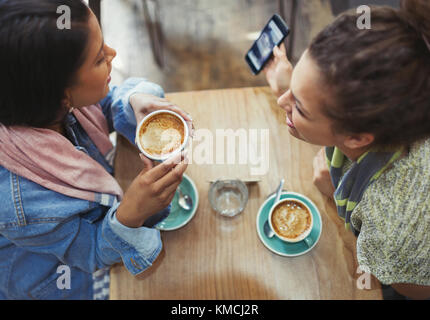 Female friends drinking coffee and using cell phone in cafe Stock Photo