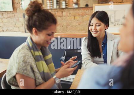 Female friends texting with cell phone in cafe Stock Photo