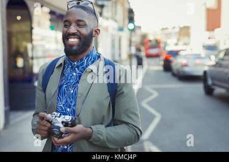 Smiling young male tourist with camera on urban street Stock Photo