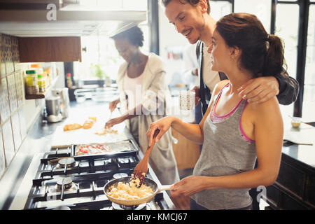Young couple cooking scrambled eggs on stove in kitchen Stock Photo