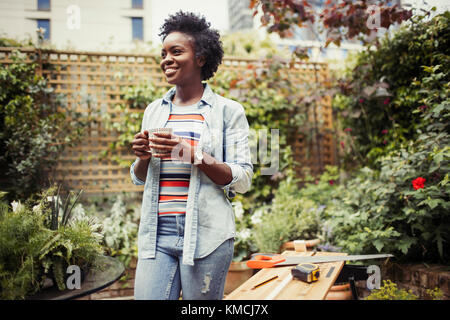 Smiling woman drinking coffee and doing DIY project on patio Stock Photo