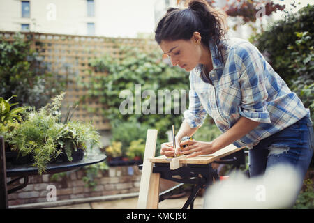 Young woman measuring and marking wood on patio Stock Photo