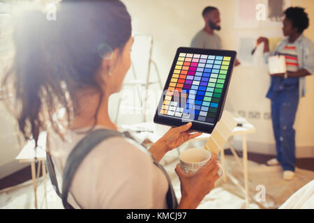 Young woman with digital tablet viewing digital paint swatches, painting living room Stock Photo
