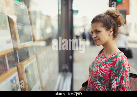 Young woman browsing real estate listings at urban storefront Stock Photo