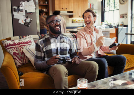 Laughing men friends playing video game on living room sofa Stock Photo