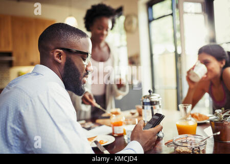 Man drinking coffee and texting with smart phone at breakfast table Stock Photo