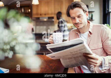 Man drinking coffee and reading newspaper in kitchen Stock Photo
