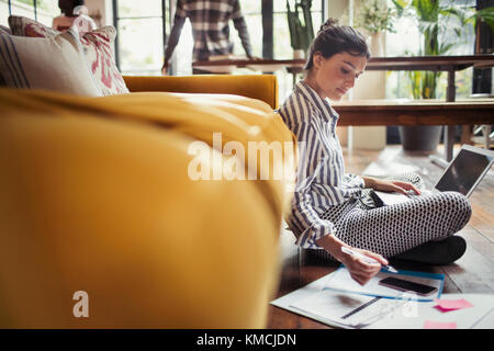 Female freelancer working at laptop on living room floor Stock Photo