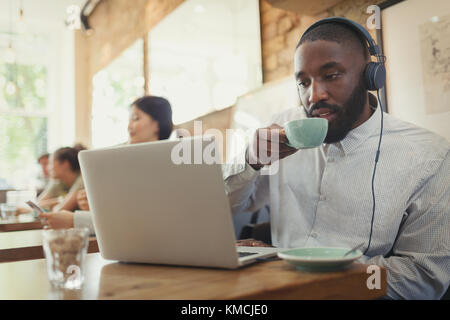 Man with headphones using laptop and drinking coffee in cafe Stock Photo