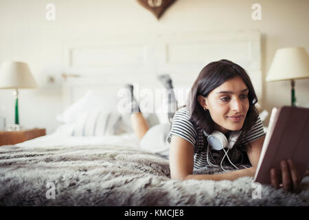 Woman with headphones relaxing on bed, using digital tablet Stock Photo