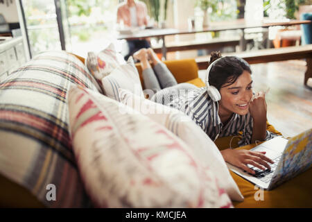 Smiling woman with headphones using laptop on sofa Stock Photo