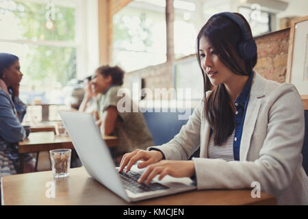 Young woman with headphones using laptop at cafe table Stock Photo