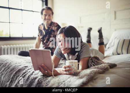 Smiling couple relaxing, drinking coffee and using digital tablet on bed Stock Photo