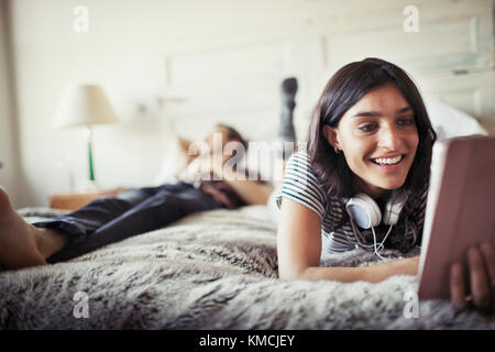 Smiling young woman with headphones using digital tablet on bed Stock Photo