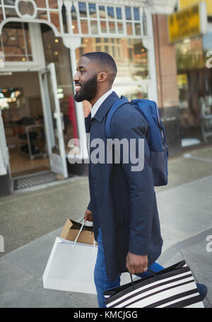 Smiling young man walking along storefront, carrying shopping bags Stock Photo