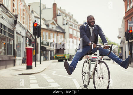 Playful young businessman commuting, riding bicycle on urban street Stock Photo