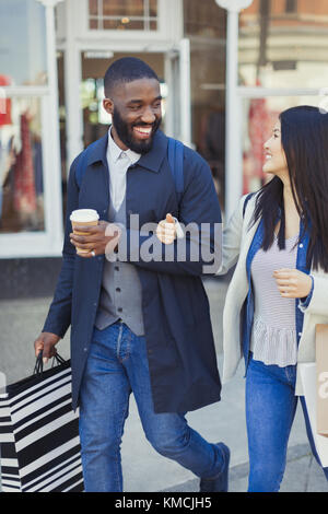 Smiling young couple walking along storefront with coffee and shopping bags Stock Photo