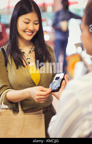 Female shopper with credit card using touchless payment in store Stock Photo