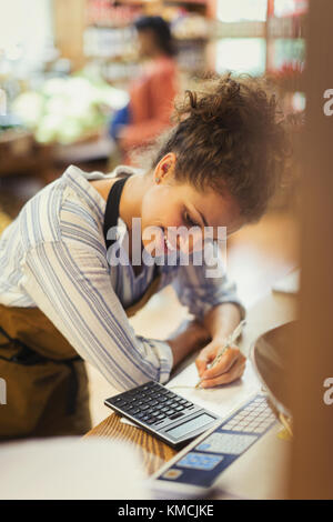 Smiling female cashier using calculator at store counter Stock Photo