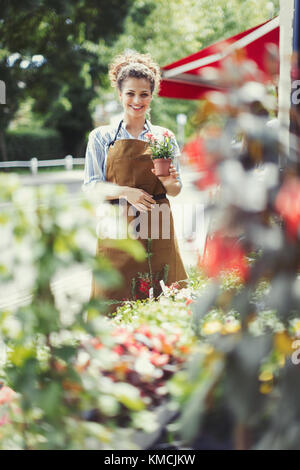 Portrait smiling female florist holding potted plant at flower shop storefront Stock Photo