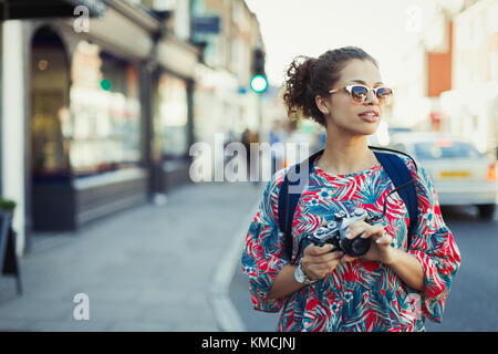 Young female tourist in sunglasses with camera on urban street Stock Photo