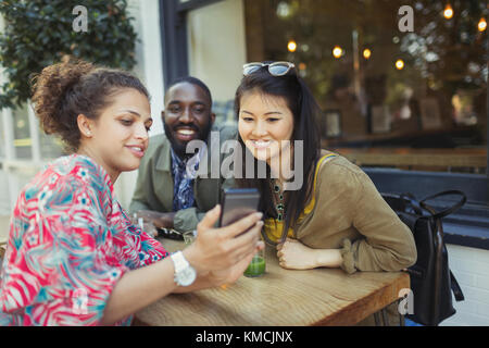 Young friends using cell phone at sidewalk cafe Stock Photo