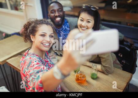 Smiling young friends taking selfie with camera phone at sidewalk cafe Stock Photo
