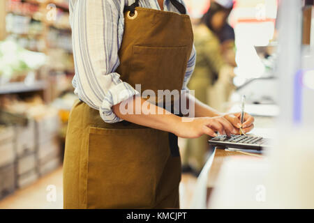 Female cashier using calculator in grocery store Stock Photo