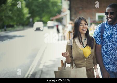 Smiling young couple with shopping bag walking on sidewalk Stock Photo