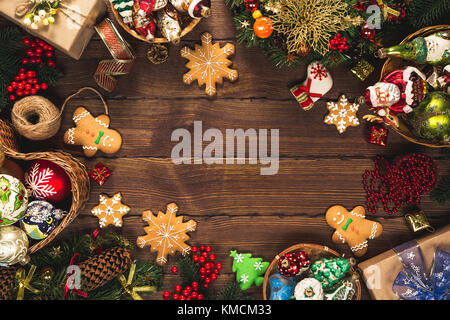 Christmas background with gifts, toys, tree branches, New Year decor, candies, and gingerbread cookies on old wooden background. Frame with free space Stock Photo